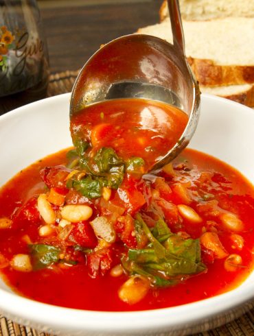 serving minestrone soup with ladle into white bowl